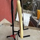 Světle žlutá elektrická kytara umístěná v černém stojanu. Na těle nástroje je vidět nečitelný nápis. Povrch laku je glossy a bez viditelných poškozen…