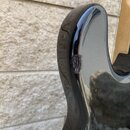 Detailní záběr na hranu černého, lakovaného trupu elektrického nástroje. Na hraně je viditelný výrazný odlak a poškození povrchu v podobě tmavého škr…