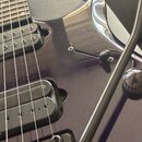 Detail elektrické kytary v tmavě fialové barvě s glossy povrchem. Na těle jsou dva černý humbuckery a černý tremolo systém s páčkou. Na základní desc…