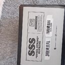 Fotografie zachycuje bílý papírový štítek nalepený na černé krabici. Na štítku je uveden nápis SSS, „STEEL STRING“ SUPREME a logo VERTEXEFFECTS.COM s…