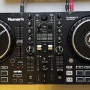 Černý DJ kontrolér značky Numark s nápisem PERFORMANCE DJ CONTROLLER a označením MIXTRAK PRO FX. Zařízení obsahuje dva velké jog-kola s bílým logem u…