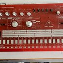 Červená analogová drum machine značky behringer s nápisem RD-6 ComputerControlled. Přístroj obsahuje řadu bílých tlačítek, několik otočných potenciom…