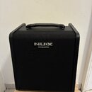 Černý akustický kombozesilovač s texturovaným povrchem a přenosnou úchytkou z umělé kůže. Na přední straně je umístěno logo NUX a pod ním nápis ACOUS…