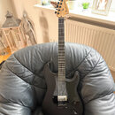 Černá elektrická kytara s jasným povrchem a světle hnědým javorovým hmatníkem. Na hlavě je viditelné logo Fender® Stratocaster®. Nástroj má jeden hum…