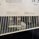 Fotografie zachycuje zadní panel kytarového zesilovače s bílou mřížkou, skrze kterou jsou vidět elektronické lampy. V horní levé části je logo "Orang…