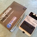 Bílé efektové pedál s černým spínacím tlačítkem a třemi ovládacími knoflíky. Na pedálu je nápis BOSS Noise Suppressor NS-2 a označení vstupů OUTPUT,…