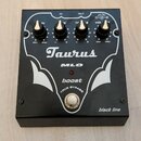 Černý kytarový efekt pedál s bílými grafickými prvky. Na horní straně jsou čtyři černé ovládací knoflíky a nápisy Taurus, MLO, boost, TRUE BYPASS a b…