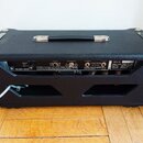 Zadní strana černého kytarového komba s koženkovým povrchem a kovovými hranami. Na zadním panelu je nápis MUSIC MAN a štítek s textem SERIAL NO. neči…