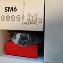 Fotografie znázorňuje krabici s nápisem SM6 a podtitulem SHOCK MOUNT WITH POP FILTER. Na krabici jsou ikony s texty MULTI-MIC COMPATIBLE, 3/8" & 5/8"…
