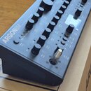 Černý syntetizátor s nápisem ARGON8M a doplňkovým textem POLYPHONIC TABLE WAVE SYNTHESIZER MODULE. Přístroj má kovové tělo s mnoha ovládacími knoflík…