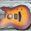 Akustická kytara s korpusem v přechodovém žlutě-hnědém odstínu (sunburst) umístěná v otevřeném tvrdém kufru s šedým polstrováním. Nástroj má hnědý hm…