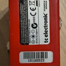 Zadní strana červeného efekt pedálu z kovu. Na černém štítku je uveden nápis tc electronic, DESIGNED IN DENMARK, MANUFACTURED IN THAILAND a technické…