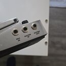 Detailní pohled na kovový panel s třemi zapuštěnými jackovými konektory. U vstupů jsou uvedeny nápisy DEC IN, GUITAR IN a GUITAR OUT. Povrch panelu v…
