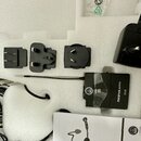 Sada příslušenství v bílém polystyrenovém obalu. Obsahuje černý bezdrátový vysílač s nápisy AKG, OMNIEL, PERCEPTION wireless a PT 45, černý napájecí…