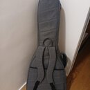 Šedý polstrovaný obal na hudební nástroj s tvarem kytary. Má dvě nastavitelné ramenní popruhy z černé tkaniny a jedno madlo v horní části. Povrch je…