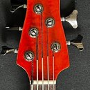Fotografie zachycuje hlavu pětstrunné basové kytary v červené barvě. V horní části je bílý nápis YAMAHA. Jsou vidět pět kovových ladiček a struny ved…
