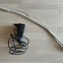 Na fotografii je bílý spirálový kabel s konektory na obou koncích a černý síťový adaptér s přívodním kabelem. Adaptér obsahuje různé technické nápisy…