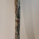 Fotografie zachycuje detail dřevěného nástroje, pravděpodobně didgeridoo. Povrch je zdoben malbou v hnědé, bílé a černé barvě s motivem hada a orname…