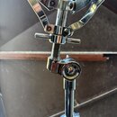 Detail chromovaného stojanu s mechanismem pro upevnění nástroje. Na kovovém kloubu je viditelný nápis TAMA. Povrch vykazuje známky běžného používání…