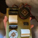 Fotografie znázorňuje elektronickou desku s osazenými součástkami, včetně kondenzátorů a dvou transformátorů. Na černých válcových kondenzátorech je…