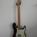 Elektrická kytara s tmele s gradací barvy od černé k hnědé a krčkem ze světlého dřeva. Na hlavě je viditelné logo Fender. Kytara má bílý pickguard, t…