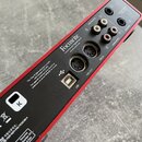 Zadní strana červeného audio rozhraní značky Focusrite. Na zařízení jsou nápisy „Focusrite“, „Focusrite Audio Engineering Ltd“ a web „www.focusrite.c…