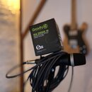 Na fotografii je černý držák na nápoje připevněný k mikrofonnímu stojanu, na kterém je svinutý černý kabel a mikrofon. Na držáku je vidět zelené logo…