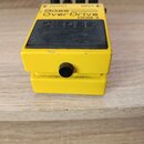 Žlutý efekt pedál s černým gumovým povrchem v horní části. Na zařízení je nápis Bass Over Drive ODB-3 a logo BOSS. V horní části jsou čtyři černé ovl…