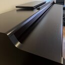Černý digitální piano v černém provedení s matným povrchem. Nástroj je vybaven přiloženým černým notovým pultem. Na povrchu nejsou vidět žádné značky…