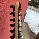 Detail hlavy kytary z profilového pohledu. Hlava je vyrobena ze světlého dřeva s černým povrchem na lícové straně a je vybavena šesti černými ladicím…