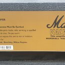 Fotografie zachycuje detail žlutého štítku na šedém, texturovaném povrchu přístroje. Na štítku je uveden nápis MODEL 8100 SOLID STATE LEAD AMPLIFIER…