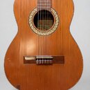 Kytara s dřevěným korpusem v přirozené hnědé barvě. Uvnitř ozvučnice je vidět štítek s nápisy „Sestet“, „classical guitar“ a „PR“. Povrch nástroje vy…