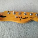 Fotografie zachycuje hlavu elektrokitary z přírodního světlého dřeva s lakovaným povrchem. Na hlavě jsou vidět nápisy „Fender“ a „TELECASTER“ a kulat…