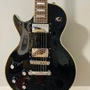 Černá elektrická kytara s tvarem singlecut a krémovým lemováním. Nástroj má dva humbuckery s chromovanými kryty, stop-bar můstek a čtyři ovládací kno…