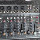 Černý mixážní pult značky behringer. Horní panel obsahuje vstupy s popisky MIC 1, MIC 2, MIC 3/4, MIC 5/6, MIC 7/8 a MIC/STEREO OUT, dále konektory L…