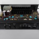 Černý stereo zesilovač s otevřeným šasi, ve kterém jsou vidět elektronické součástky, kondenzátory a chladič. Na předním panelu je nápis TESLA STEREO…