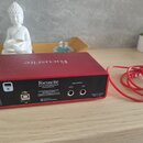 Červené audio rozhraní značky Focusrite s nápisem Focusrite na horní straně. Na zadním panelu je uveden název Focusrite, text Focusrite Audio Enginee…