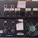 Fotografie zobrazuje zadní strany dvou černých rackových zesilovačů. Horní zařízení má nápisy INPUT B, INPUT A, OUTPUT B a OUTPUT A u konektorů, vpra…