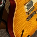 Detail elektrické kytary s žlutou flamed maple deskou a červeným bokem. Na těle jsou vidět dva snímače s krémovými rámečky a kovový most. Kytara je u…