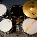 Sada bubnů a jeden činel v tmavě hnědé barvě. Na blanách jsou viditelné nápisy EVANS a na činelu značka Zildjian s označením CUSTOM. K sadě patří bas…