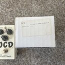 Bílá krabička s papírovou nálepkou, na které je text „OCD“, „po: 437341“, „Fulltone OCD Obsessive Compulsive Drive“ a vpravo dole kód „16852A2“. Vedl…