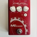 Červený efekt pedál s nápisy MIC, OUT a POWER v horní části. Na zařízení je bílé logo TC HELICON a tři bílé otočné ovladače s popisky ECHO (TAPE, DIG…