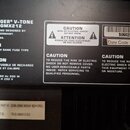 Fotografie detailu zadní strany černého přístroje. Je zde vidět bílý text s označením BEHRINGER® V-TONE MODEL GMX212, nápisy CONCEIVED AND DESIGNED B…