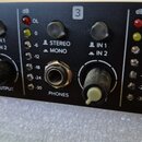 Detailní záběr na černý ovládací panel audio zařízení. Jsou zde viditelné nápisy dB, OL, 0, -6, -12, -18, -24, -30, STEREO, MONO, IN 1, IN 2 a PHONES…