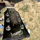 Detail hlavy černé elektrické kytary s nápisy „Les Paul“ a „MODEL“. Ve spodní části je viditelné logo „Gibson“. Povrch je glossy, s viditelnými odles…