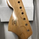 Zadní strana dřevěné hlavy kytary v přírodní barvě s lakovaným povrchem. Na dřevě je černý nápis „Designed and Backed by Fender“, pod ním označení „s…