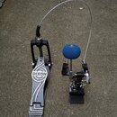 Černý basový pedál s kovovým šlapadlem, na kterém je bílý nápis DIXON. K pedálu vede flexibilní kovové táhlo k mechanismu u bubnu. Mechanismus je vyb…