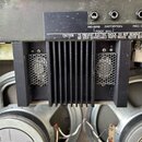 Detail vnitřku komba s dvěma reproduktory a černým chladičem. Na horním panelu jsou tři konektory s popisky REVERB, DISTORTION a REC. OUT, pod nimi n…