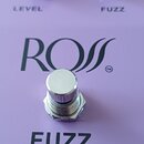 Fialový efekt pedál s dvěma černými oválnými ovladači, pod kterými jsou nápisy LEVEL a FUZZ. Uprostřed je velký nápis ROSS s obchodní značkou ™ a pod…