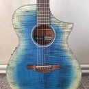 Akustická kytara s modrým gradientem a viditnou strukturou dřeva. Uvnitř ozvučovacího otvoru je štítek s nápisy „Ibanez“, „MODEL: AEG-20“ a „MADE IN…